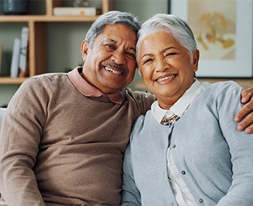 smiling elderly couple embracing while sitting on a couch